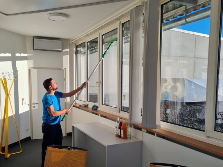 Reinigungskraft bei der materialgerechten Bearbeitung einer Glasfläche im Innenraum mit viel Tageslicht